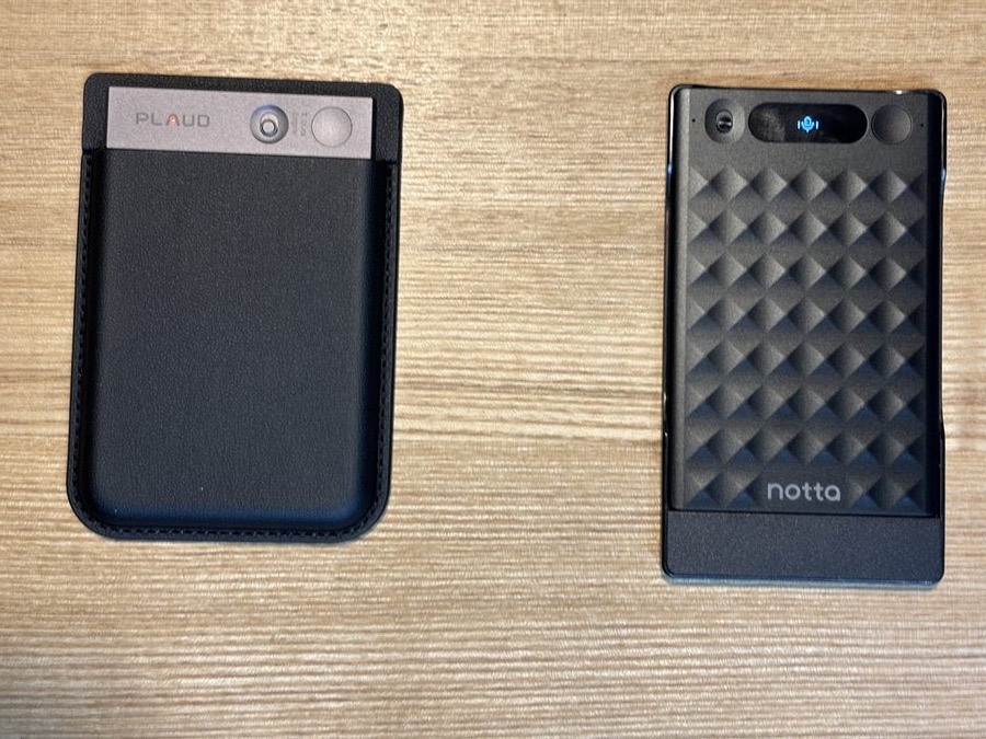 机の上に並べたNotta Memo（左・青いランプが点灯）とPLAUD Note（右・ケースに入り赤いランプが点灯）。どちらも録音中