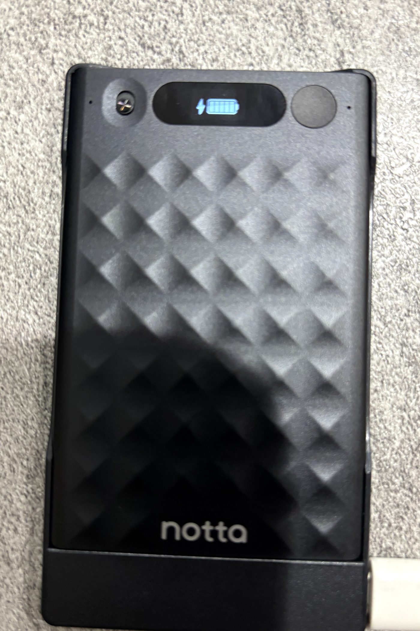 Notta Memoをケースに入れたままUSB-Cケーブルで充電している様子（画面にバッテリーと充電アイコン）